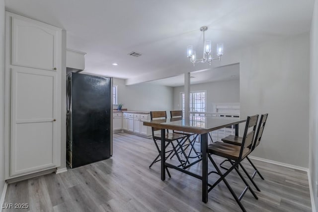 dining space featuring light wood finished floors, an inviting chandelier, visible vents, and baseboards