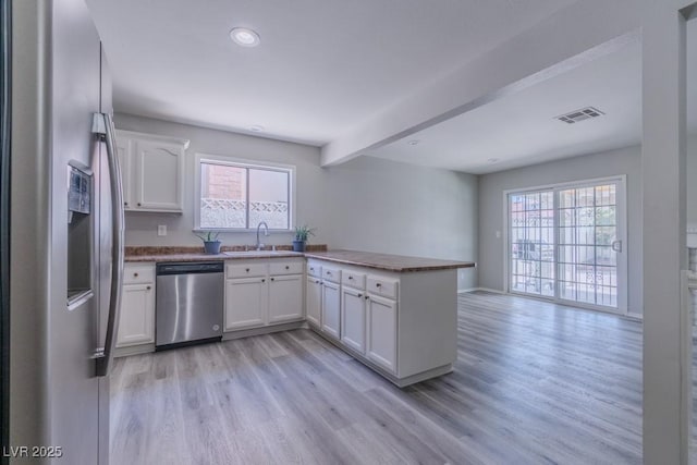 kitchen with light wood finished floors, visible vents, a sink, a peninsula, and stainless steel appliances