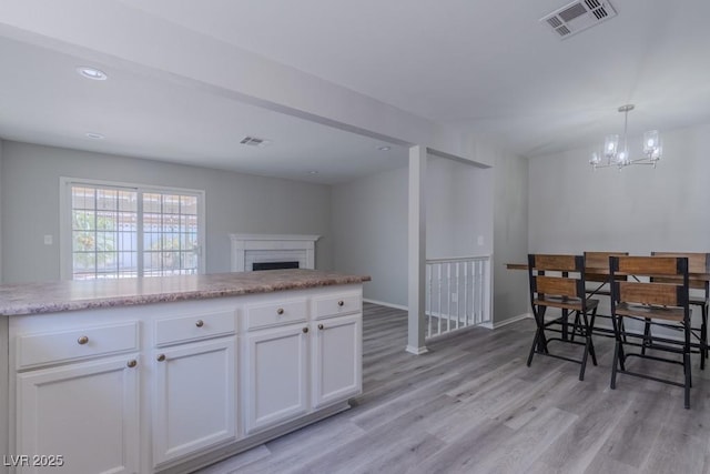 kitchen featuring light wood finished floors, an inviting chandelier, a fireplace, white cabinetry, and visible vents