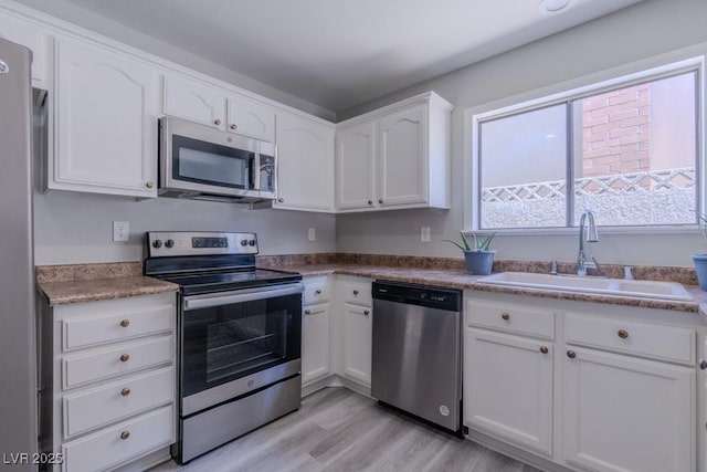kitchen featuring white cabinets, stainless steel appliances, light wood finished floors, and a sink