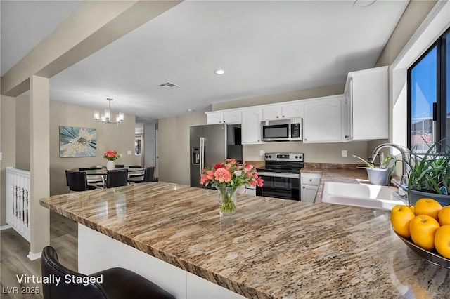 6361 W Viking Rd, Las Vegas, NV 89103 - kitchen with stainless steel appliances, a sink, white cabinets, a chandelier, and recessed lighting