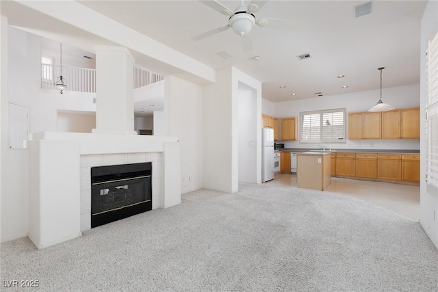 unfurnished living room with ceiling fan, light colored carpet, visible vents, a sink, and a tiled fireplace