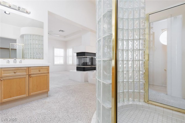full bathroom with a walk in shower, vanity, visible vents, and a multi sided fireplace
