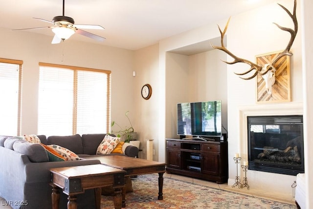 living area featuring a glass covered fireplace and ceiling fan