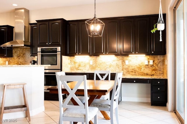kitchen with double oven, light stone counters, light tile patterned floors, and wall chimney range hood