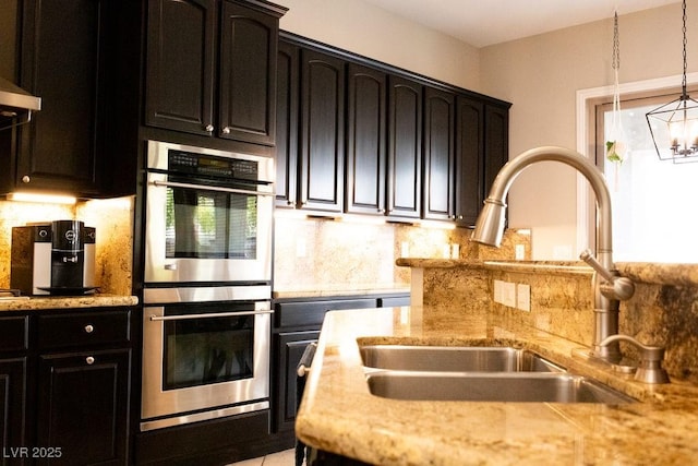 kitchen with tasteful backsplash, dark cabinets, stainless steel double oven, and a sink