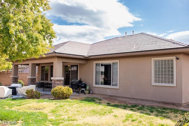 rear view of property featuring a tile roof, a patio area, stone siding, a yard, and stucco siding