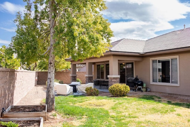 rear view of house with a tiled roof, a fenced backyard, a patio area, a lawn, and stucco siding
