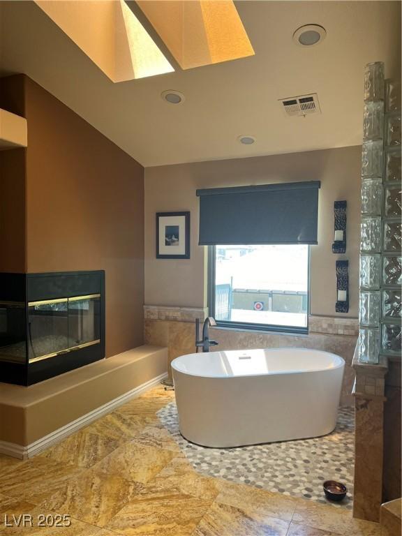 8690 W Ford Ave, Las Vegas, NV 89148 - bathroom featuring a freestanding bath, tile walls, a skylight, a multi sided fireplace, and a wainscoted wall