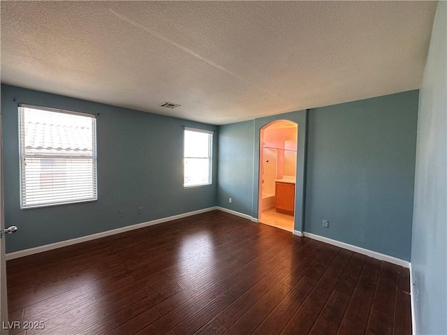 unfurnished room with dark wood-style flooring, visible vents, baseboards, and arched walkways