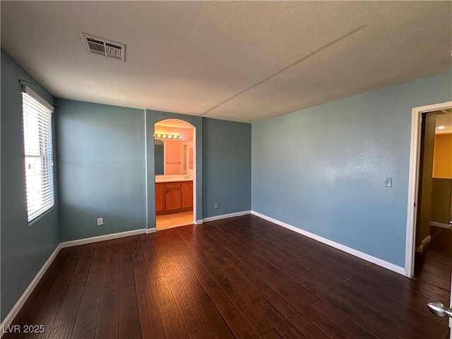 empty room with baseboards, a textured ceiling, visible vents, dark wood finished floors, and arched walkways