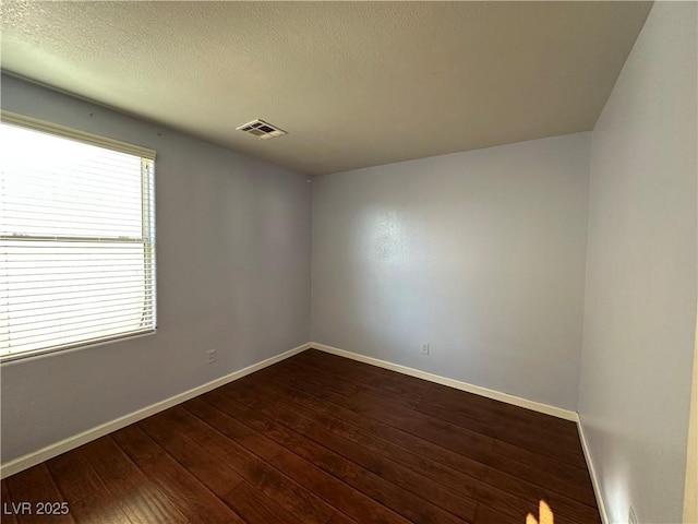 empty room with visible vents, baseboards, a textured ceiling, and dark wood-style floors