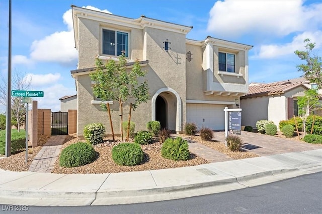 view of front facade with a gate, stucco siding, an attached garage, and driveway
