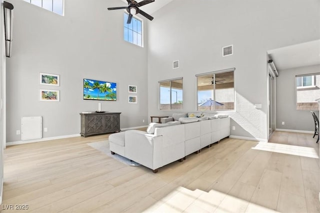 living room featuring a ceiling fan, a towering ceiling, light wood-style floors, and baseboards