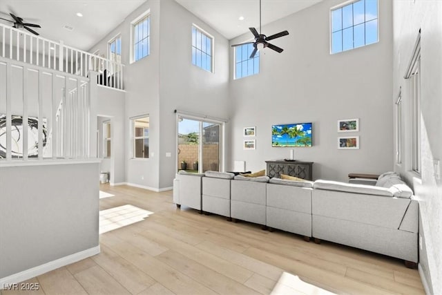 living area with ceiling fan, a high ceiling, wood finished floors, healthy amount of natural light, and recessed lighting