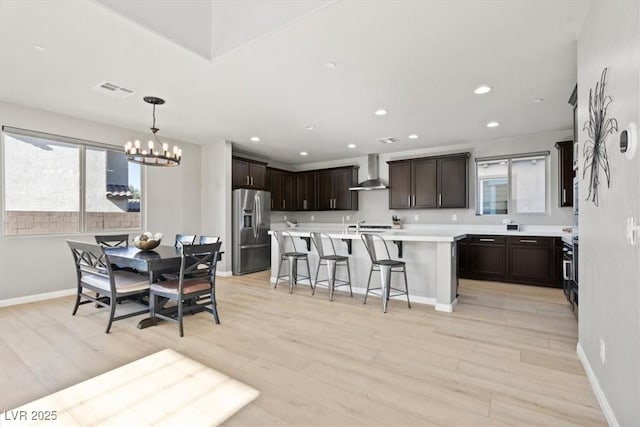 kitchen featuring stainless steel fridge, wall chimney range hood, a chandelier, a breakfast bar area, and light countertops