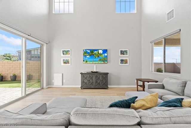 living area with a towering ceiling, light wood-style flooring, and baseboards