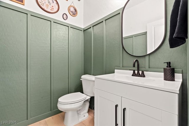 bathroom featuring a decorative wall, toilet, vanity, and a wainscoted wall