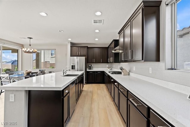 kitchen featuring light countertops, light wood finished floors, a chandelier, recessed lighting, and a kitchen island with sink