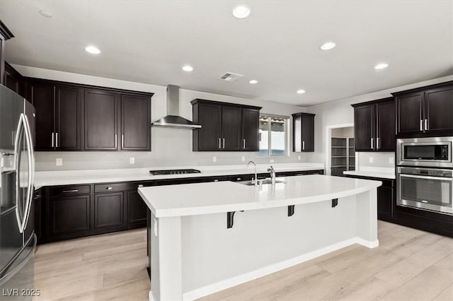 3062 Echoed Rondel Ln, Henderson, NV 89044 - kitchen with appliances with stainless steel finishes, wall chimney range hood, a center island with sink, light wood-style floors, and a kitchen breakfast bar