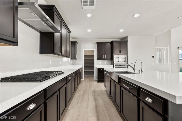 3062 Echoed Rondel Ln, Henderson, NV 89044 - kitchen featuring appliances with stainless steel finishes, wall chimney range hood, light wood finished floors, a center island with sink, and recessed lighting