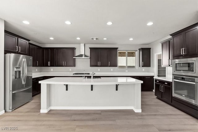3062 Echoed Rondel Ln, Henderson, NV 89044 - kitchen featuring appliances with stainless steel finishes, wall chimney exhaust hood, light wood-style flooring, a center island with sink, and recessed lighting