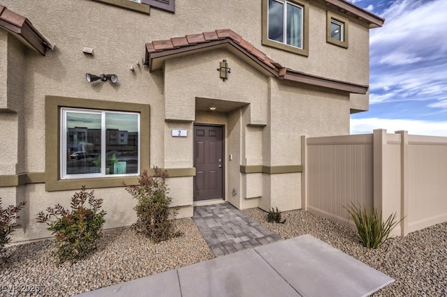 view of exterior entry with a tiled roof, stucco siding, and fence