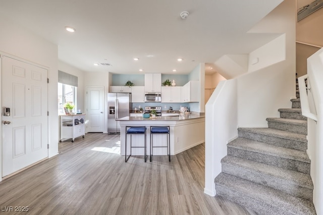 kitchen with a breakfast bar, light wood-style floors, white cabinetry, and appliances with stainless steel finishes