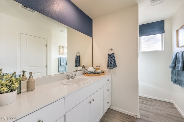 bathroom with vanity, visible vents, baseboards, and wood finished floors