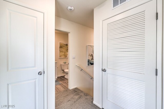 hallway with an upstairs landing, visible vents, and carpet