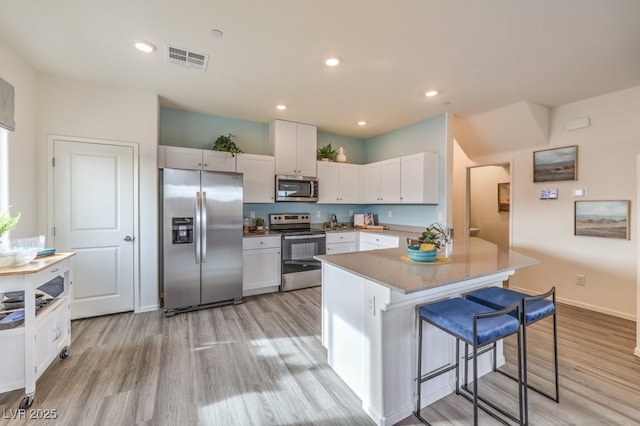 kitchen featuring white cabinets, light wood-style floors, visible vents, a kitchen bar, and stainless steel appliances
