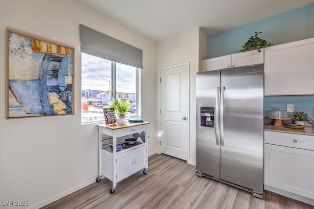 kitchen with light wood finished floors, stainless steel fridge with ice dispenser, baseboards, and white cabinetry