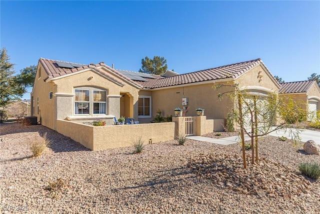 back of property with stucco siding, a tiled roof, solar panels, and a fenced front yard