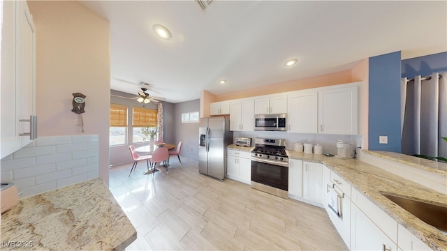 kitchen featuring a ceiling fan, appliances with stainless steel finishes, light stone counters, and white cabinetry