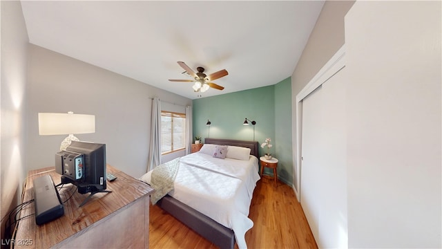 bedroom featuring light wood finished floors, ceiling fan, a closet, and a wood stove