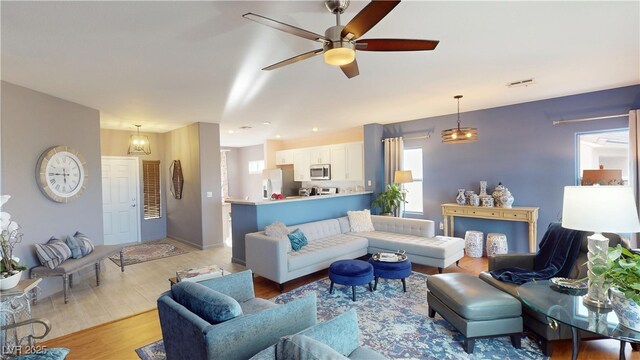 living area featuring light wood-type flooring, baseboards, ceiling fan, and plenty of natural light