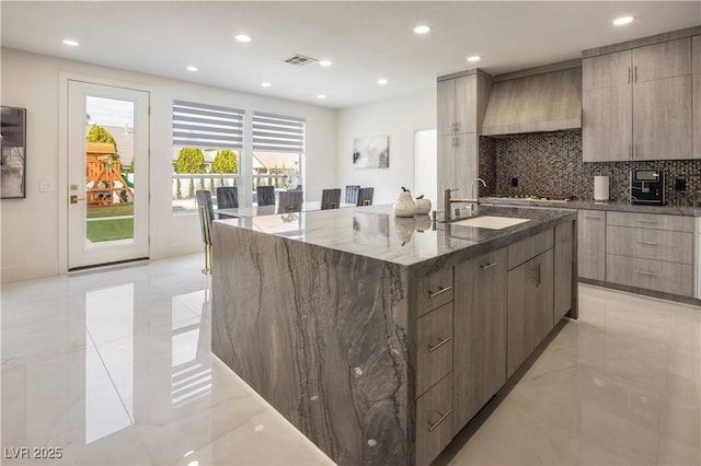 kitchen with modern cabinets, a sink, dark stone countertops, a large island, and decorative backsplash