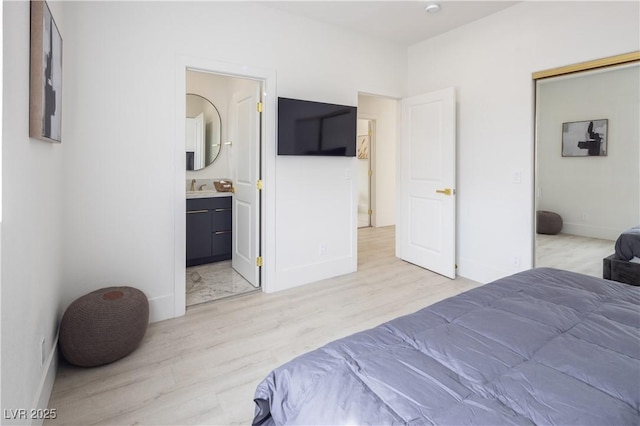 bedroom featuring light wood finished floors, a sink, baseboards, and connected bathroom