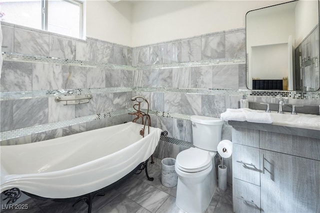 full bathroom with tile walls, toilet, a freestanding tub, vanity, and marble finish flooring