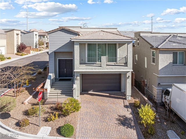 view of front of home with a garage, fence, stucco siding, a residential view, and decorative driveway