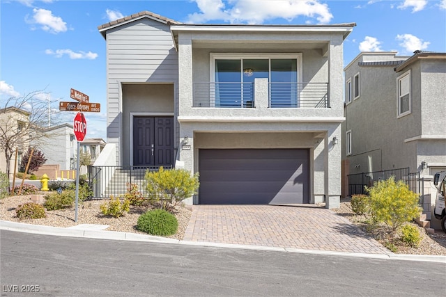 view of front facade featuring stucco siding, decorative driveway, fence, a balcony, and a garage