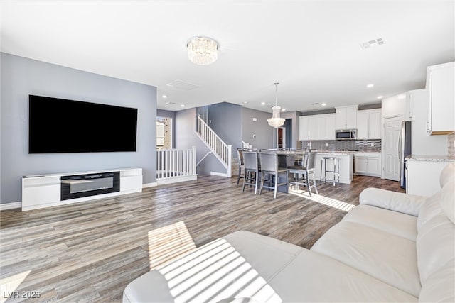 living area with visible vents, baseboards, light wood finished floors, recessed lighting, and stairs