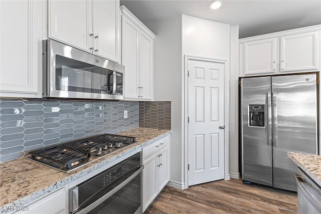 kitchen featuring tasteful backsplash, white cabinets, appliances with stainless steel finishes, dark wood-style flooring, and light stone counters
