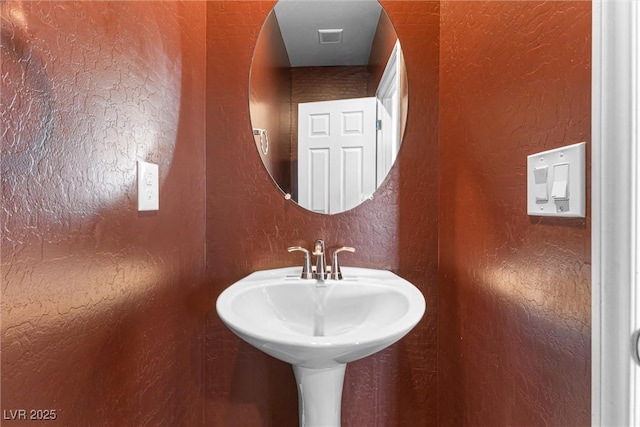 bathroom featuring a textured wall, a sink, and visible vents