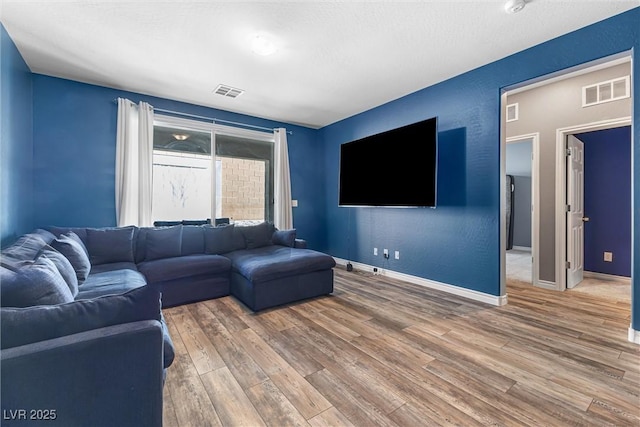 living area with wood finished floors, baseboards, and visible vents