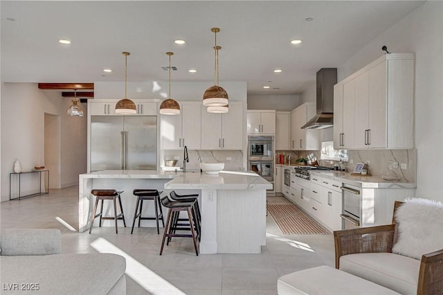 12199 Canyon Sunset St, Las Vegas, NV 89138 - kitchen featuring wall chimney exhaust hood, a large island with sink, white cabinetry, appliances with stainless steel finishes, and decorative backsplash
