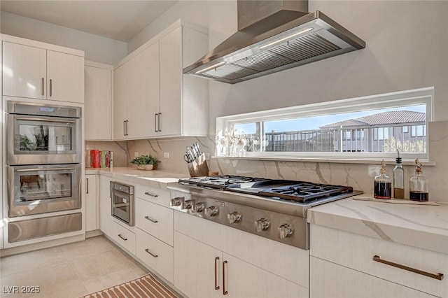 12199 Canyon Sunset St, Las Vegas, NV 89138 - kitchen with a warming drawer, backsplash, light stone countertops, wall chimney exhaust hood, and stainless steel appliances