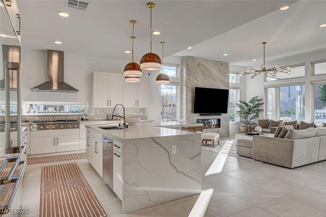 12199 Canyon Sunset St, Las Vegas, NV 89138 - kitchen with a sink, wall chimney range hood, a chandelier, stainless steel gas stovetop, and a center island with sink