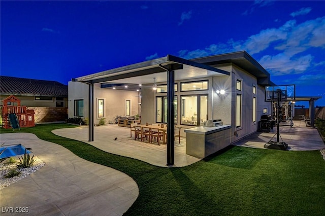 12199 Canyon Sunset St, Las Vegas, NV 89138 - back of house at twilight featuring a patio area, stucco siding, a playground, and a lawn