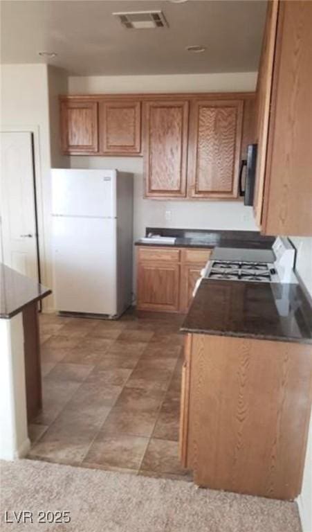 kitchen with visible vents, brown cabinets, freestanding refrigerator, and dark countertops
